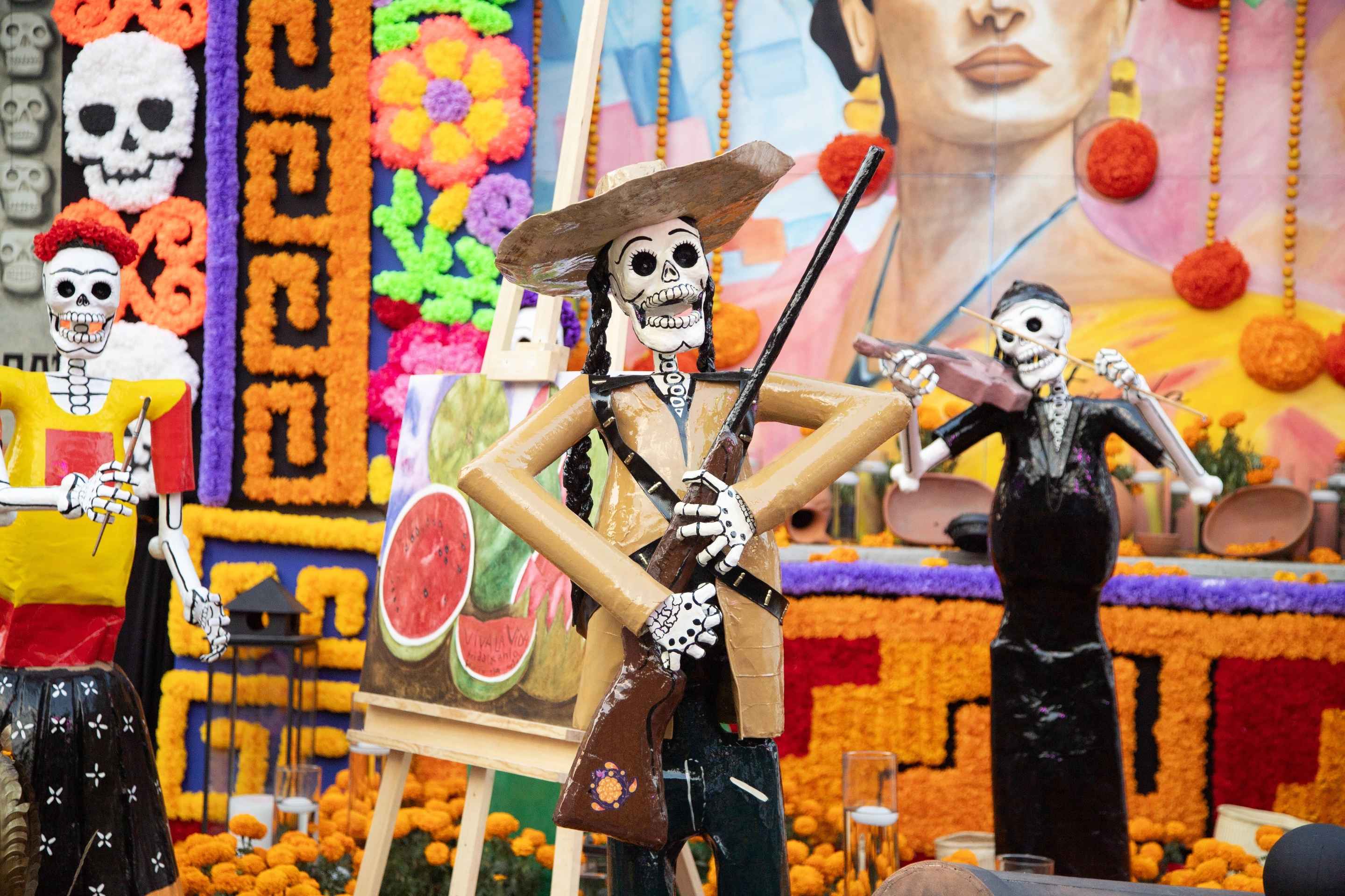Figurines de squelettes mexicains en costume, parmi des fleurs orange et des fruits