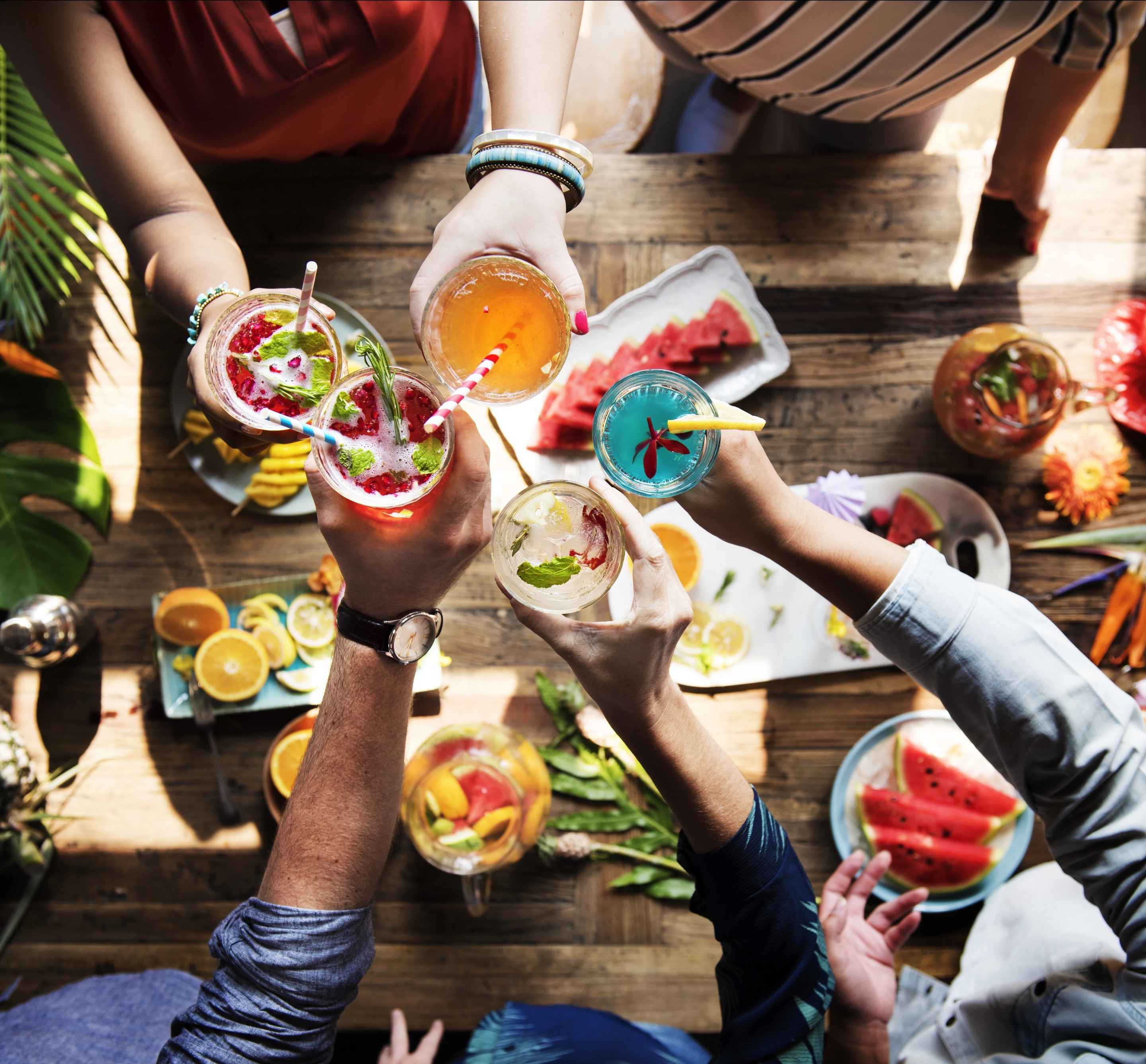 Mains qui trinquent avec des cocktails colorés au-dessus d’une table garnie